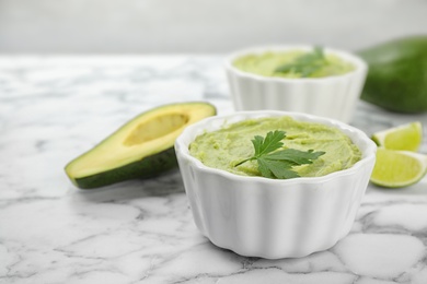 Photo of Bowls of guacamole with cut avocado and lime on marble table, space for text