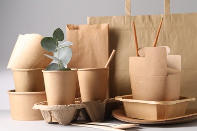 Photo of Eco friendly food packaging. Paper containers, tableware, bag and eucalyptus branch on white table