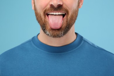 Man showing his tongue on light blue background, closeup