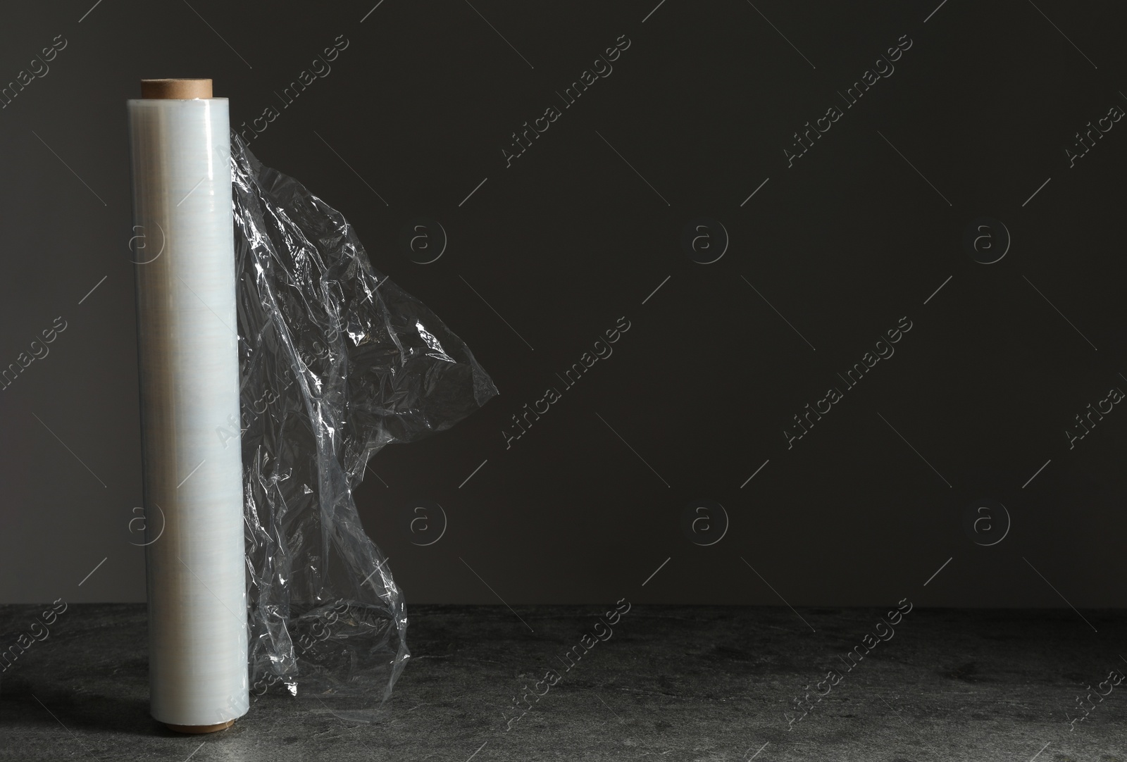 Photo of Roll of plastic stretch wrap film on table against black background, space for text