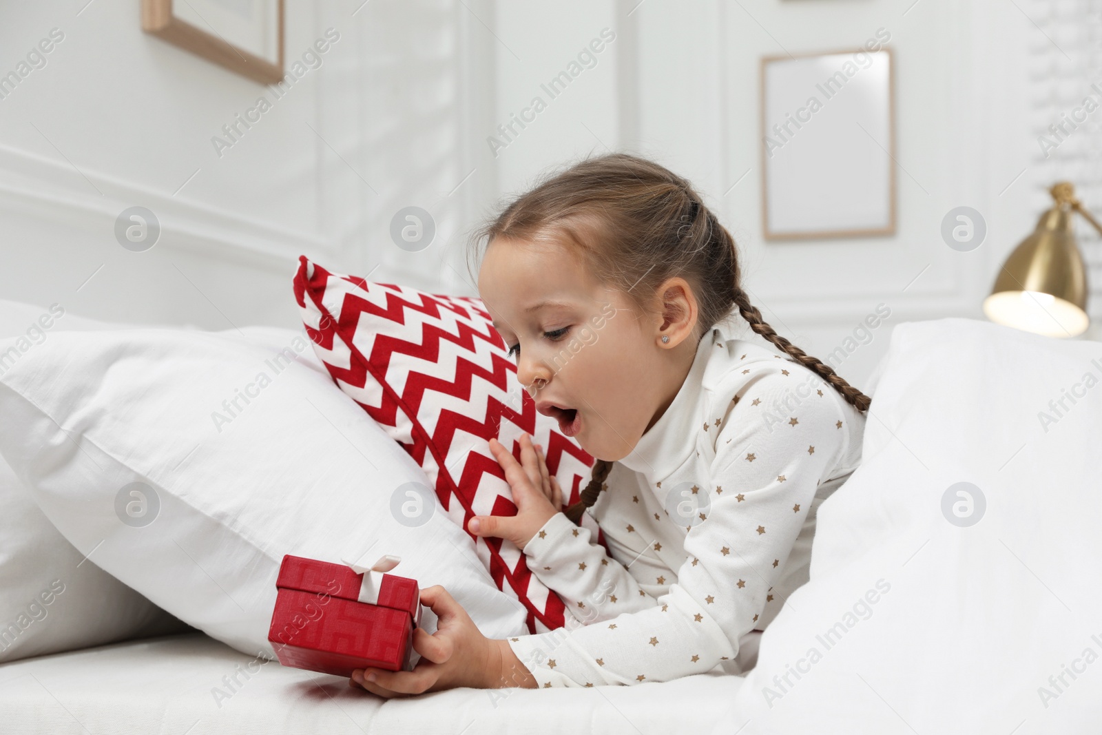 Photo of Excited little girl finding gift box under pillow in bed at home. Saint Nicholas day tradition