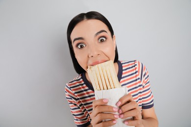 Photo of Emotional young woman eating delicious shawarma on grey background