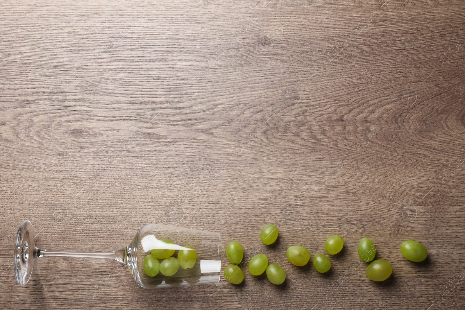 Photo of Wineglass with scattered grapes on wooden table, flat lay. Space for text