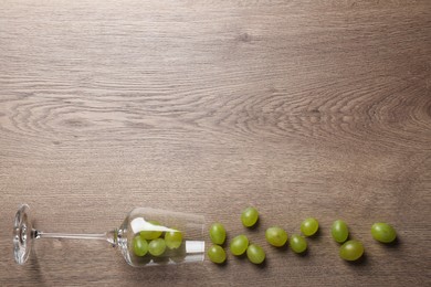 Wineglass with scattered grapes on wooden table, flat lay. Space for text