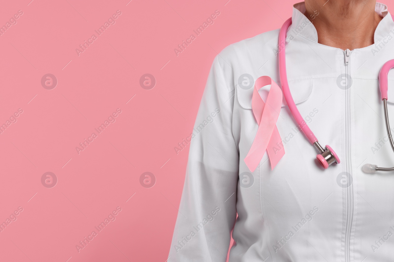 Photo of Doctor with pink ribbon and stethoscope on color background, closeup and space for text. Breast cancer awareness