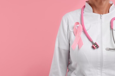 Photo of Doctor with pink ribbon and stethoscope on color background, closeup and space for text. Breast cancer awareness