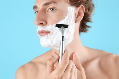 Handsome young man shaving on color background