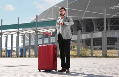Photo of Being late. Worried businessman with red suitcase and passport outdoors