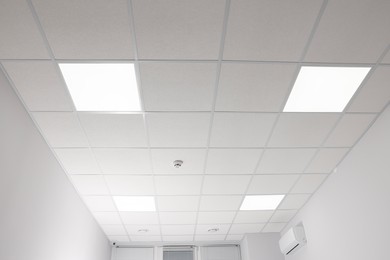 Photo of White ceiling with PVC tiles and lighting indoors, low angle view