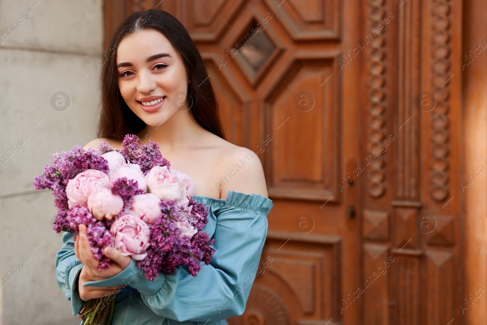 Photo of Beautiful woman with bouquet of spring flowers near building outdoors, space for text