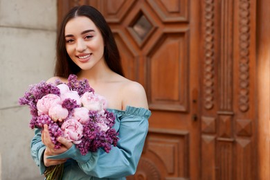 Photo of Beautiful woman with bouquet of spring flowers near building outdoors, space for text