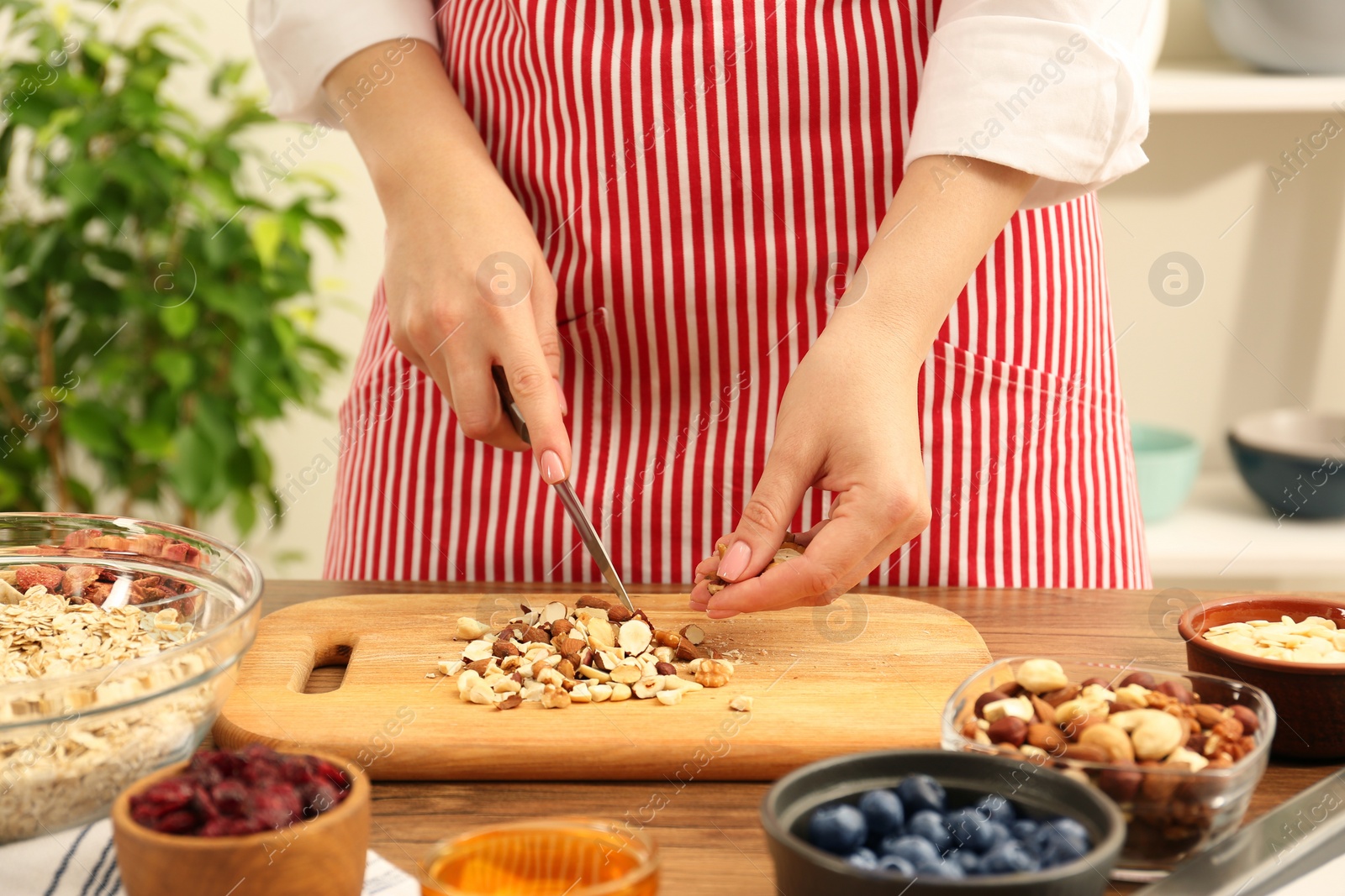 Photo of Making granola. Woman cutting nuts at table in kitchen, closeup