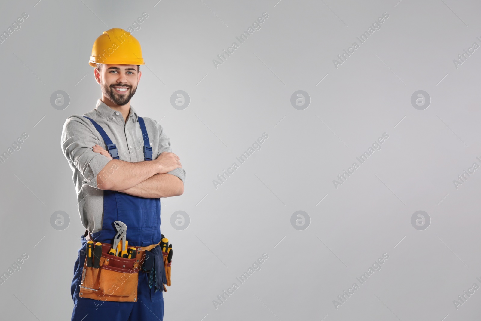 Photo of Portrait of professional construction worker with tool belt on grey background, space for text