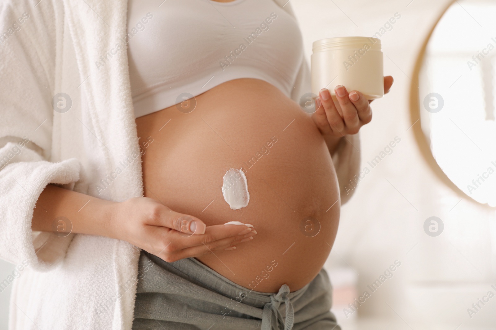 Photo of Young pregnant woman with cosmetic product in bathroom, closeup