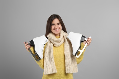 Happy woman with ice skates on grey background