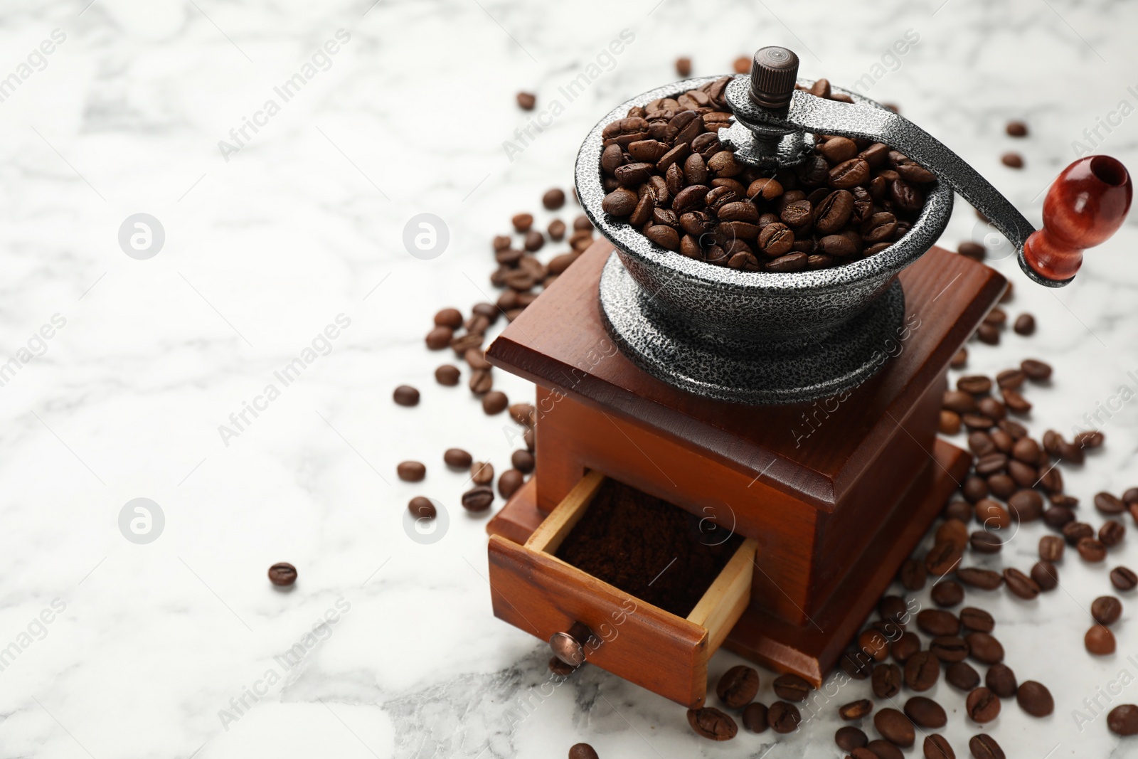 Photo of Vintage manual coffee grinder with beans on white marble table. Space for text