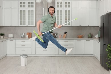 Enjoying cleaning. Man in headphones jumping with mop in kitchen