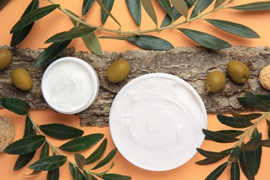 Flat lay composition with jars of cream and olives on pale orange background