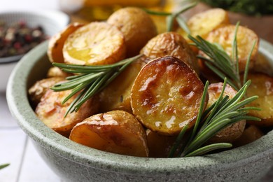 Photo of Tasty baked potato and aromatic rosemary in bowl on table, closeup