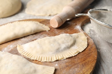 Raw chebureki with tasty filling and rolling pin on wooden table, closeup
