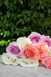 Photo of Beautiful bouquet of roses on light grey table outdoors, closeup