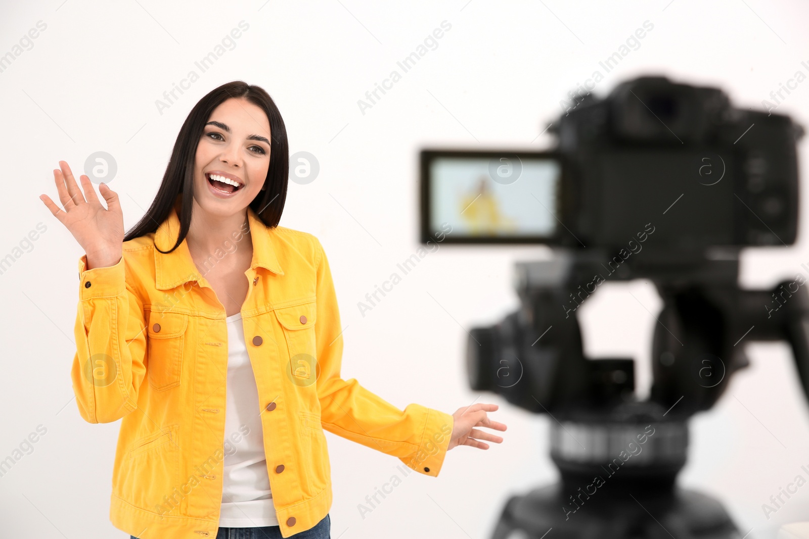 Photo of Young blogger recording video on camera against white background