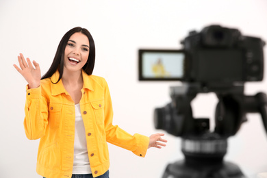 Photo of Young blogger recording video on camera against white background