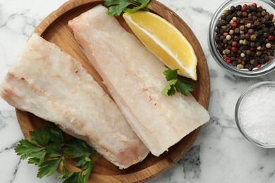 Photo of Fresh raw cod fillets, spices and lemon on white marble table, flat lay