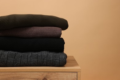 Photo of Stack of casual sweaters on wooden table against light brown background. Space for text