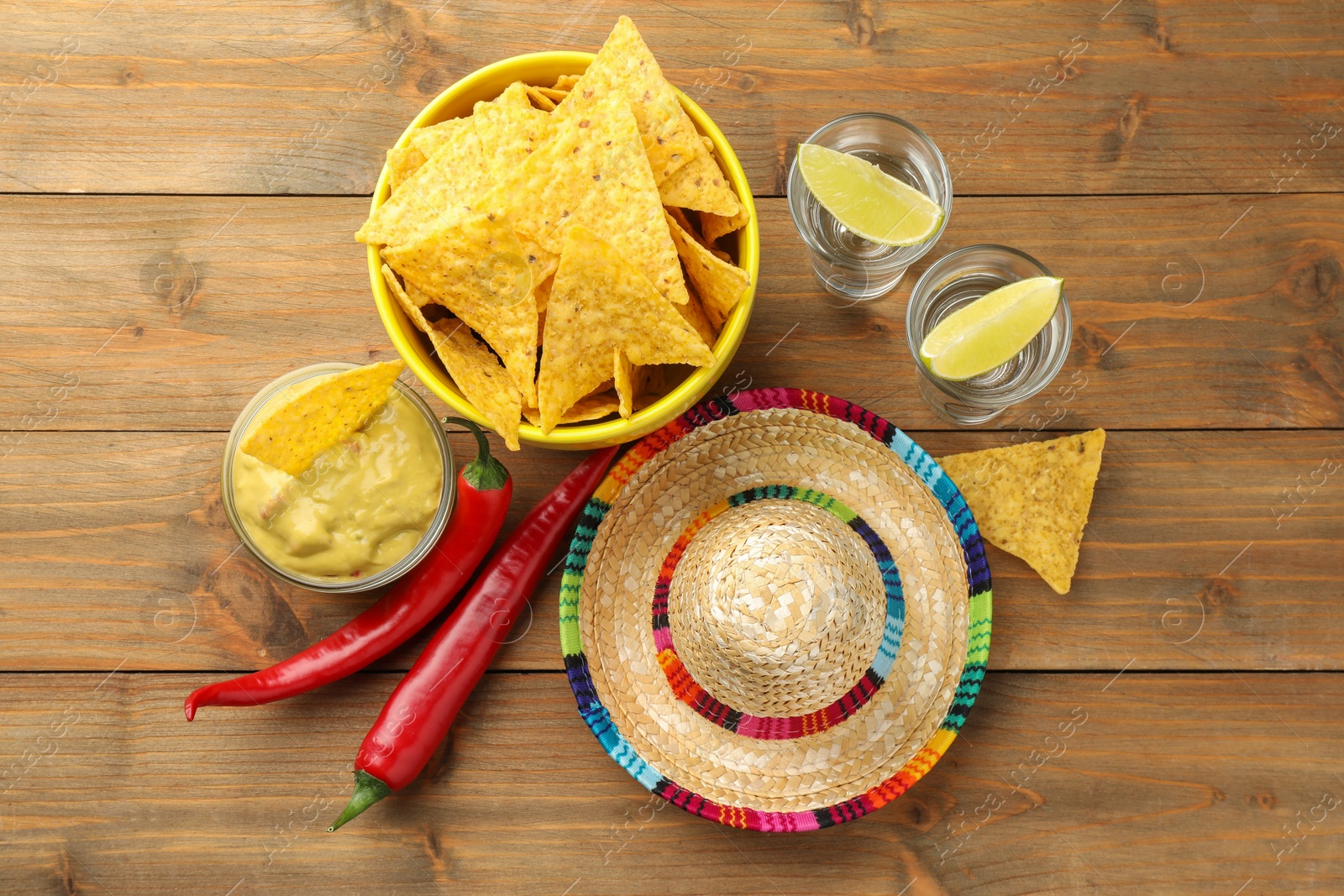 Photo of Mexican sombrero hat, tequila, chili peppers, nachos chips and guacamole on wooden table, flat lay