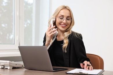 Happy secretary talking on phone at table in office