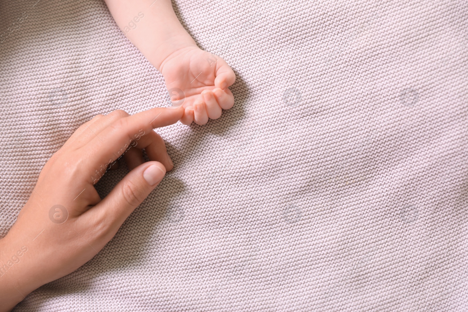 Photo of Mother and her newborn baby on light grey knitted plaid, top view. Space for text