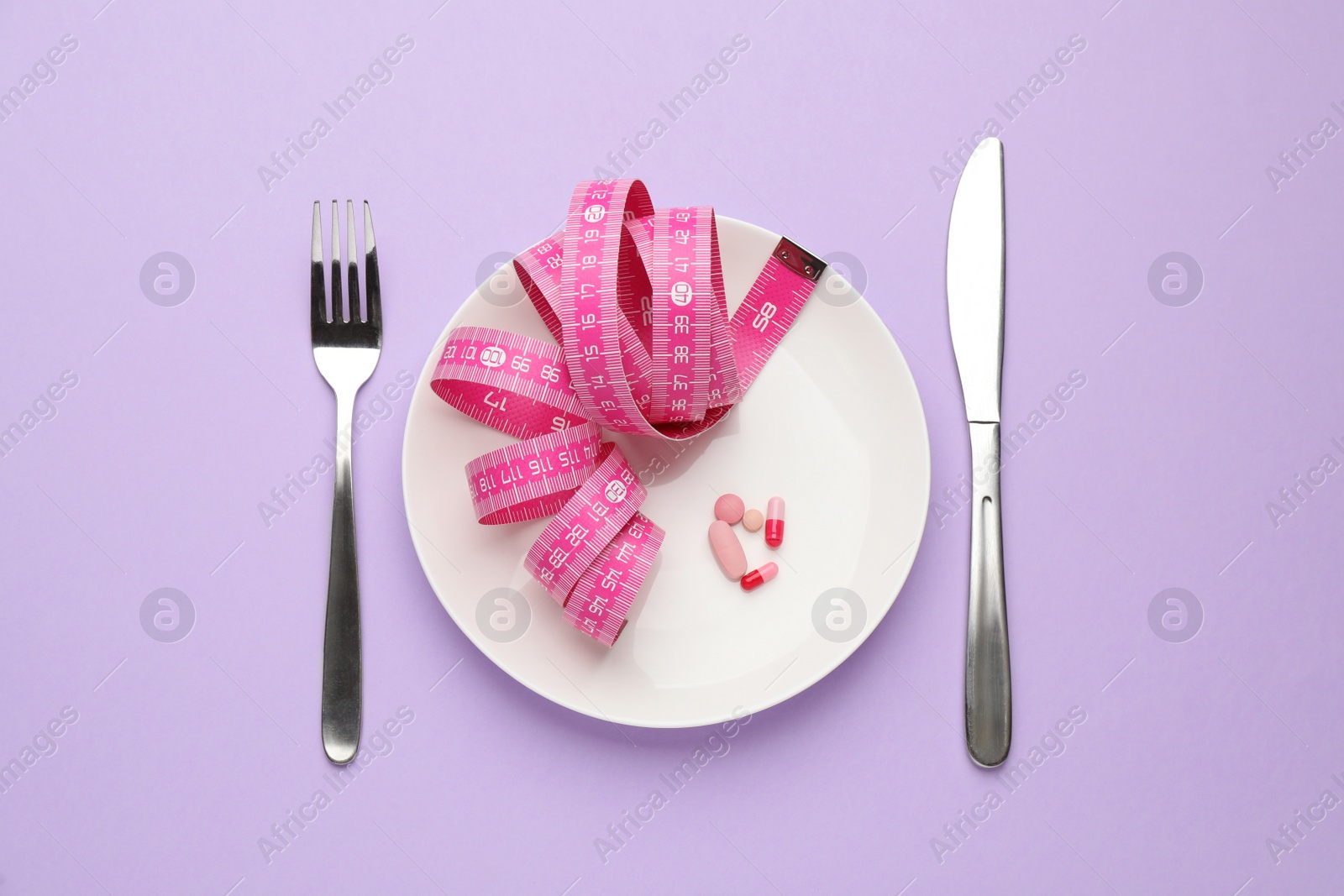 Photo of Plate with weight loss pills, measuring tape and cutlery on violet background, flat lay