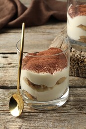 Photo of Delicious tiramisu in glasses and spoon on wooden table