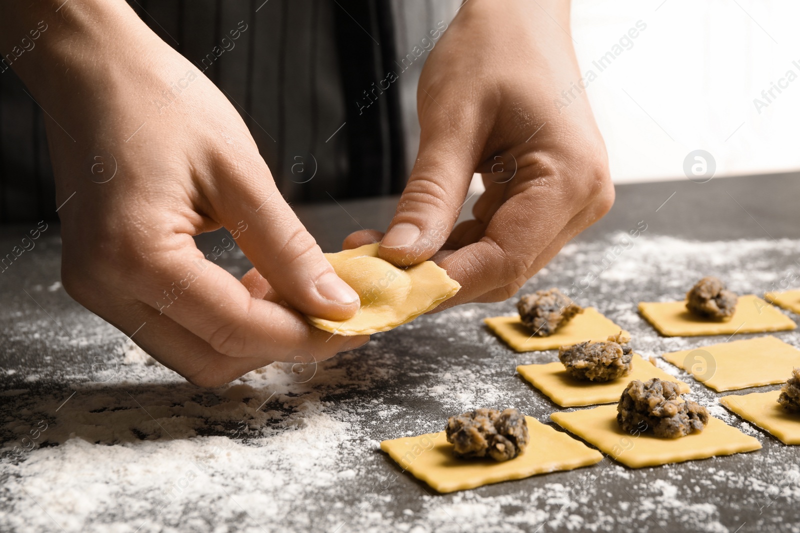 Photo of Woman making ravioli at grey table, closeup. Italian pasta