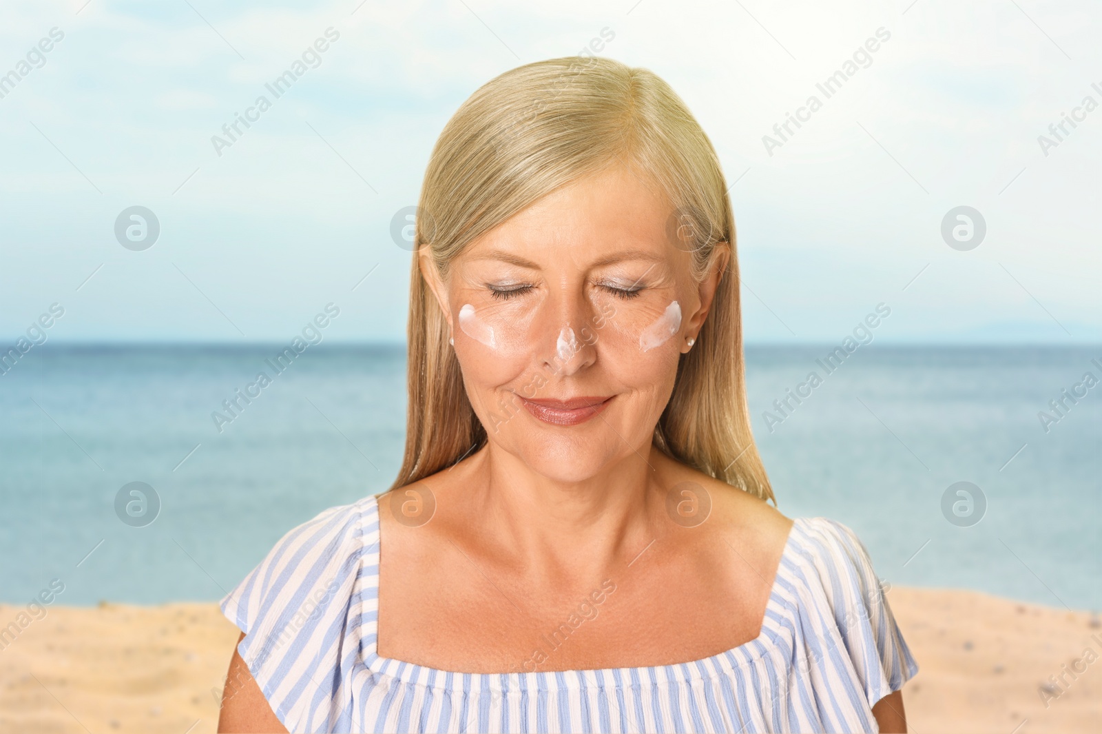 Image of Sun protection. Beautiful young woman with sunblock on her face near sea