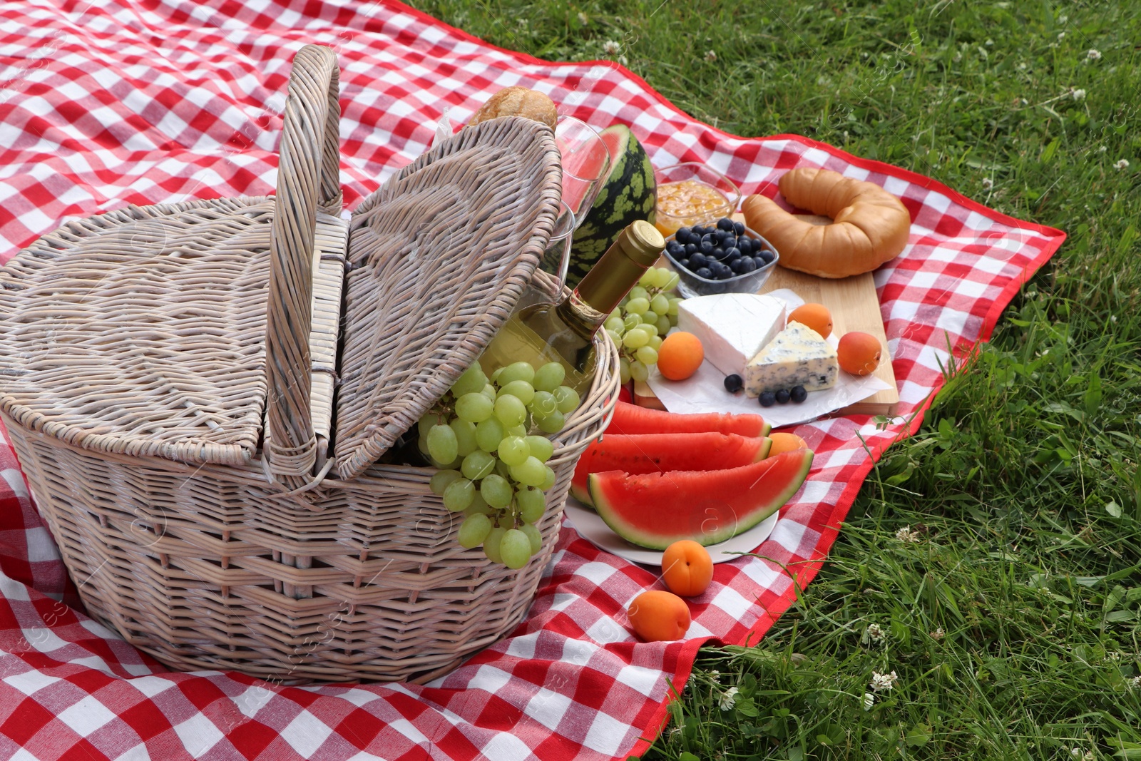 Photo of Picnic blanket with delicious food and wine outdoors on summer day