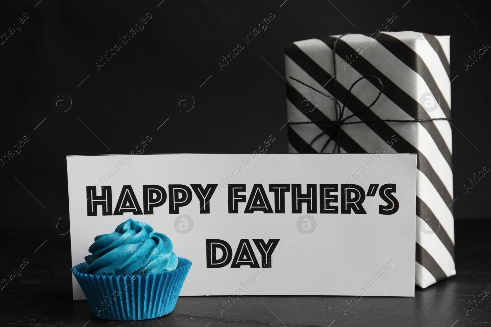 Photo of Cupcake, gift box and card with phrase HAPPY FATHER'S DAY on black table