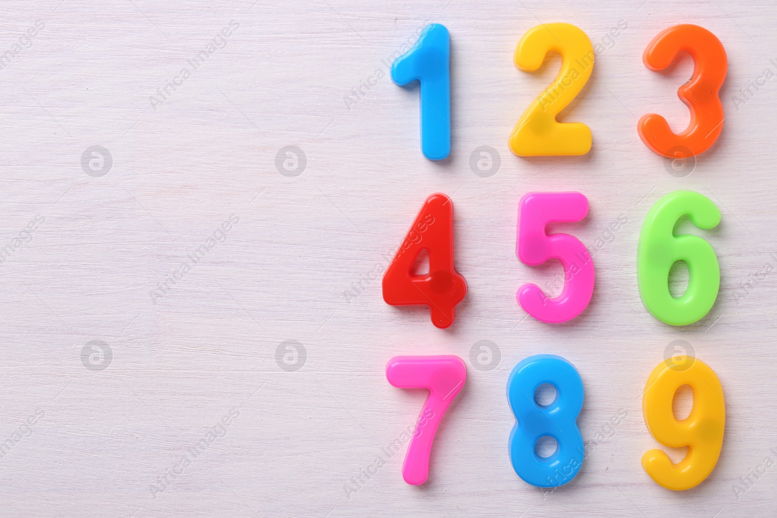 Photo of Colorful numbers on white wooden school desk, flat lay. Space for text