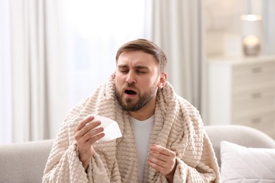 Photo of Young man suffering from runny nose in living room