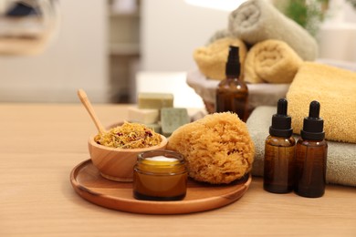 Photo of Dry flowers, bottles of essential oils, loofah and jar with cream on wooden table indoors. Spa time