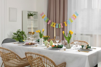 Photo of Festive Easter table setting with painted eggs, burning candles and yellow tulips in room