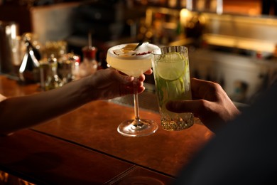 Photo of People clinking glasses with fresh cocktails at bar counter, closeup
