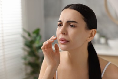 Photo of Woman with dry skin checking her face indoors, space for text