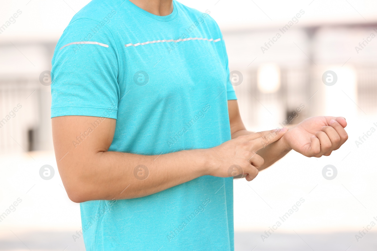 Photo of Young man checking pulse outdoors on sunny day