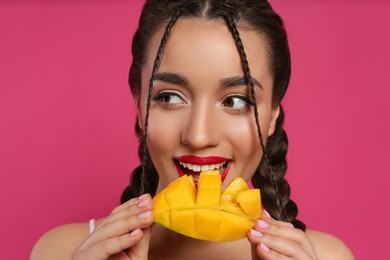 Photo of Young woman eating fresh mango on pink background. Exotic fruit