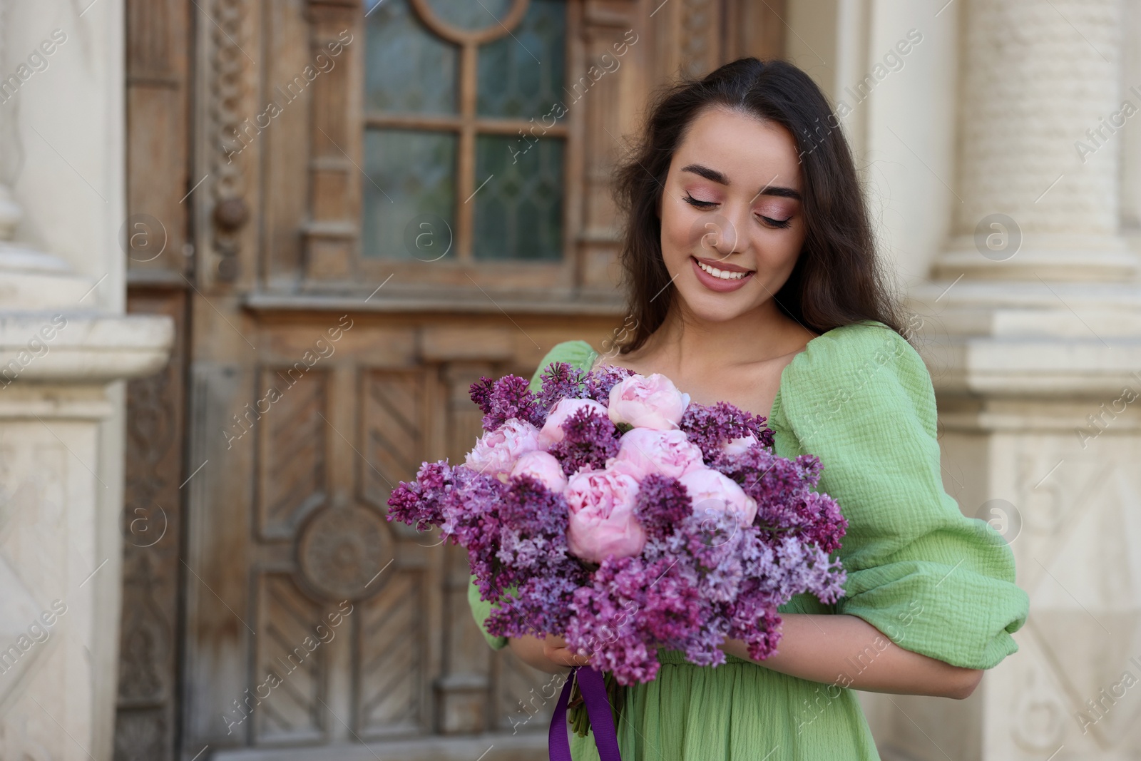 Photo of Beautiful woman with bouquet of spring flowers near building outdoors, space for text