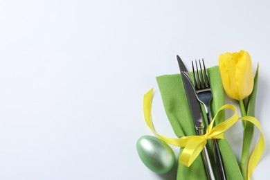 Photo of Cutlery set, Easter egg and tulip on white background, top view with space for text. Festive table setting