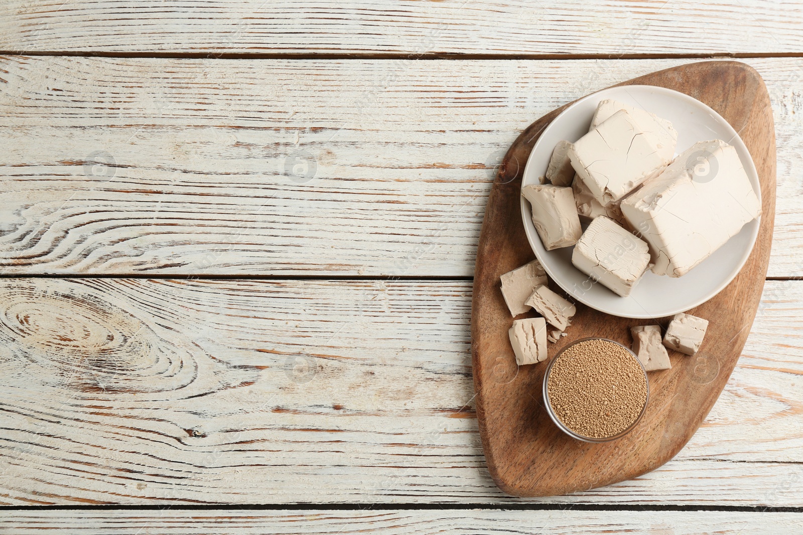 Photo of Compressed and granulated yeast on white wooden table, top view. Space for text