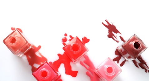 Photo of Spilled different nail polishes with bottles on white background, top view